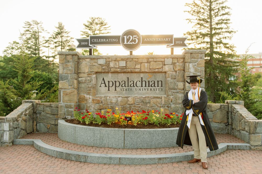 Graduate poses at Appalachian State University 125th anniversary stone entrance sign.