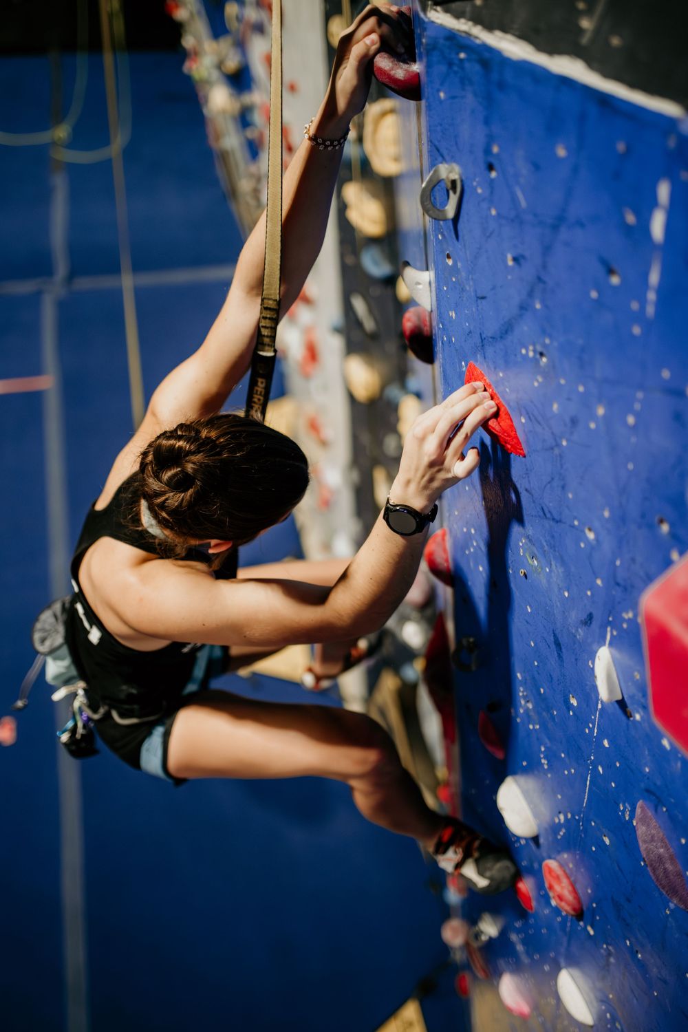 Athletic climber ascending blue indoor climbing wall with colorful holds.