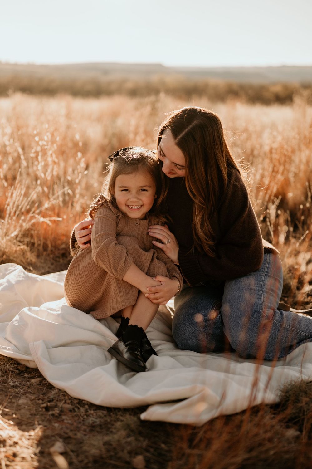 Mother and child sharing tender moment on blanket in sunlit field.
