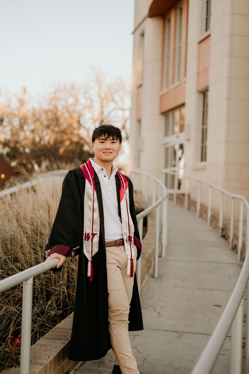Student wearing graduation stole poses on campus steps during golden hour.