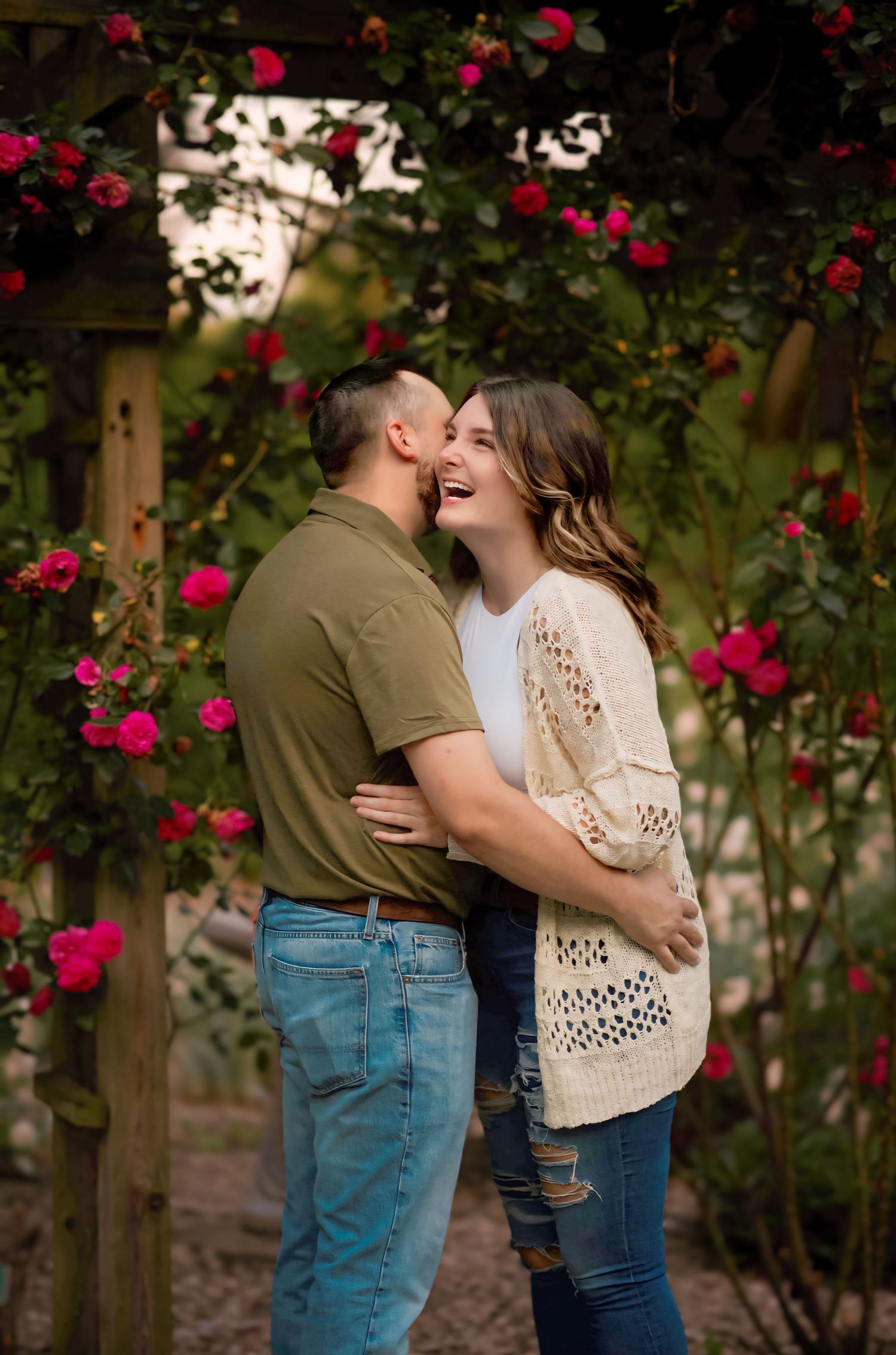 Happy couple laughing and embracing under a blooming red rose garden arbor outdoors.