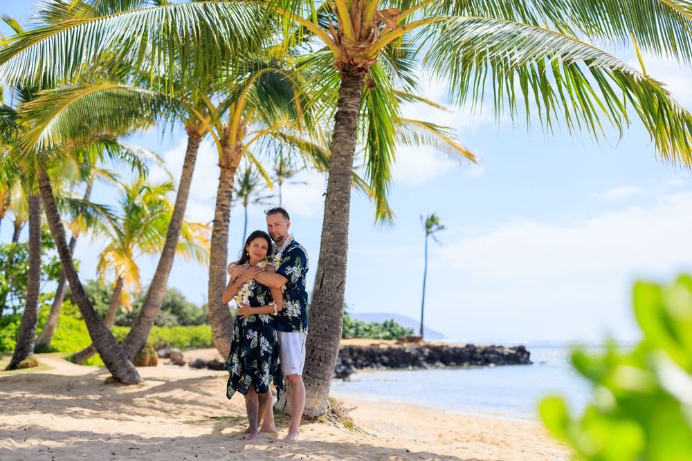 Couple embracing on a tropical Hawaiian beach surrounded by palm trees with ocean views on a sunny day.