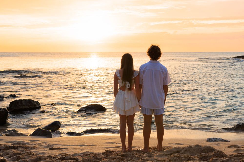 Couple holding hands on a sandy beach watching a golden sunset over the ocean.