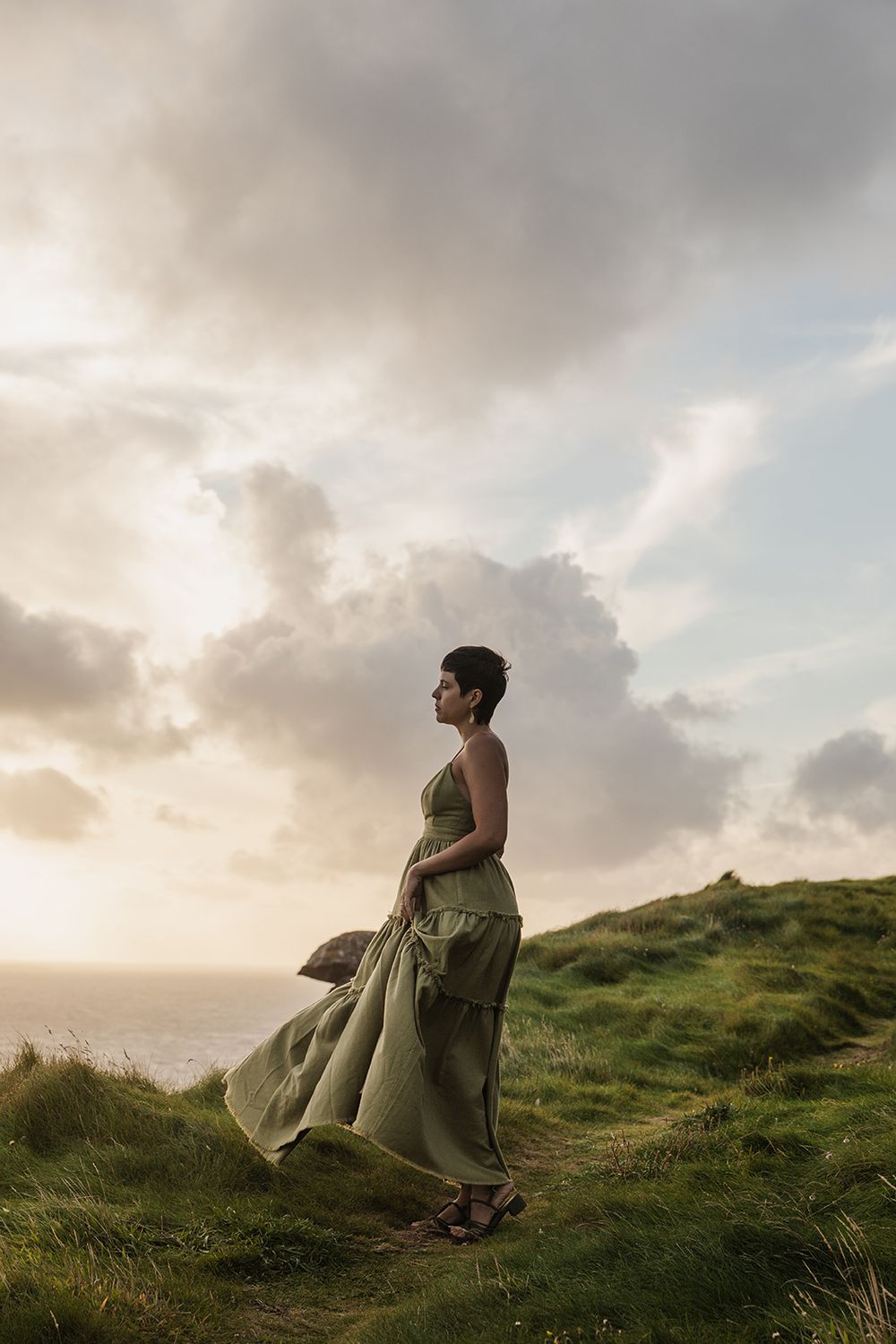 woman in a long green dress is standing at the edge of Cliffs of Moher during her adventurous portrait photo session