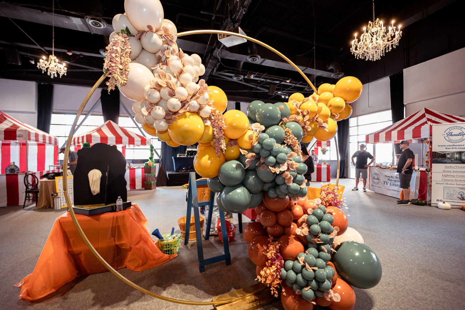 Carnival-themed venue with elaborate balloon decorations in orange and teal against striped backdrop.