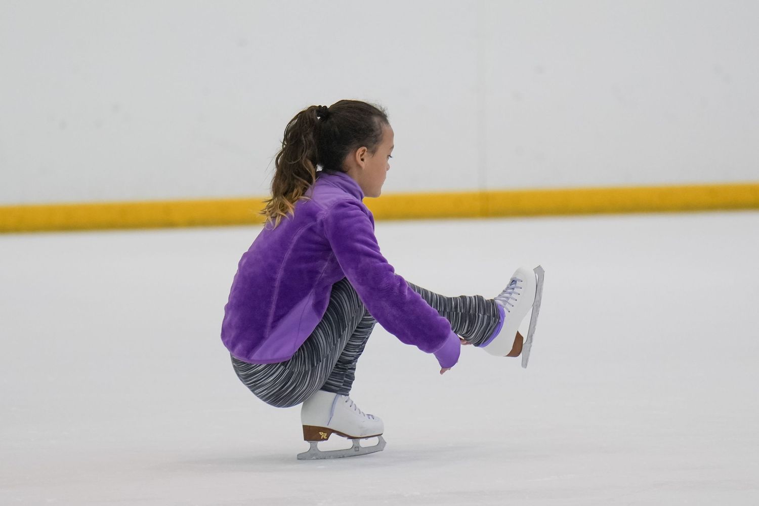 Figure skater in purple performing a crouching move on ice.