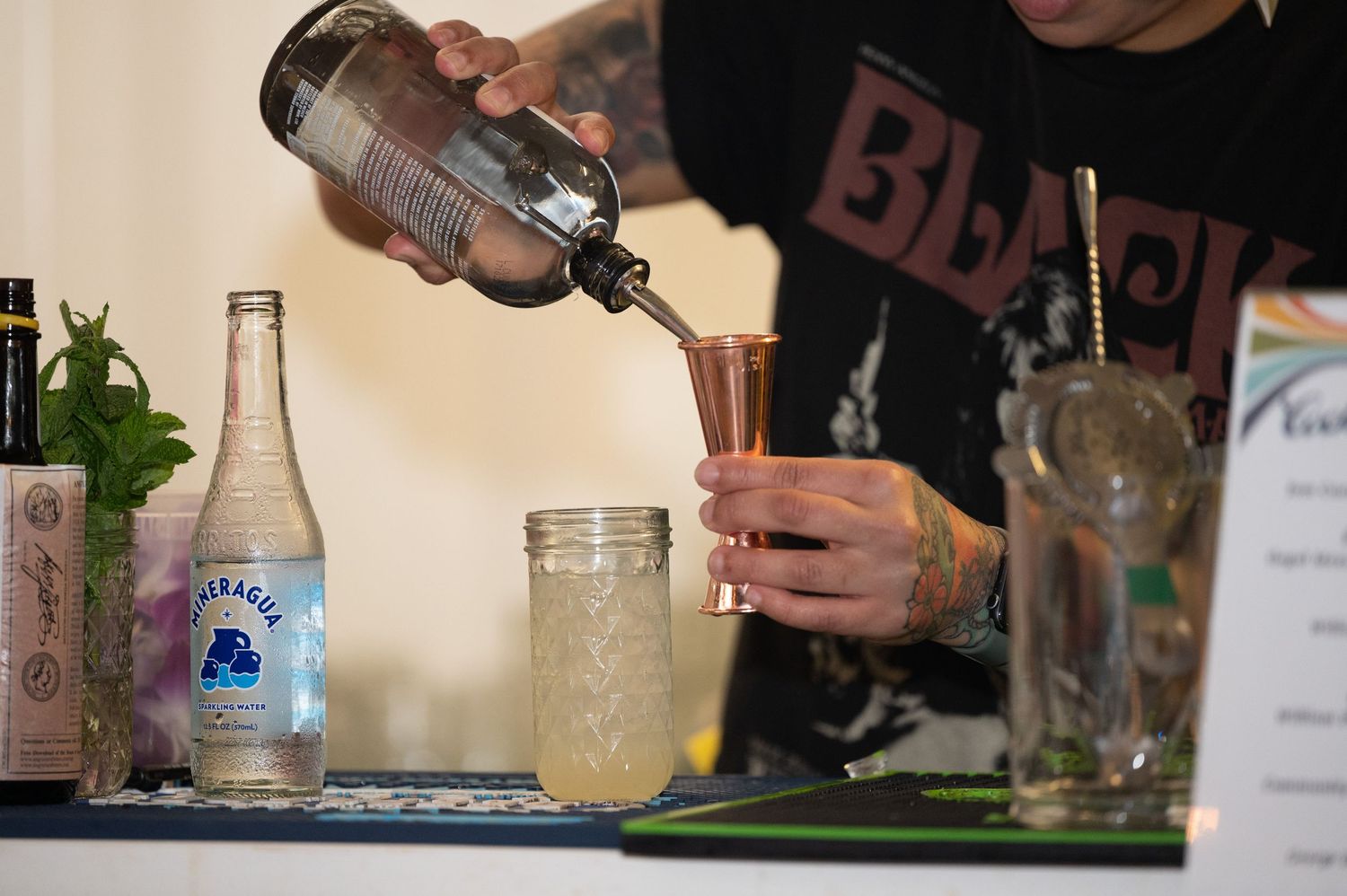 Hands pouring drinks and mixing cocktails at a professional bar setup.