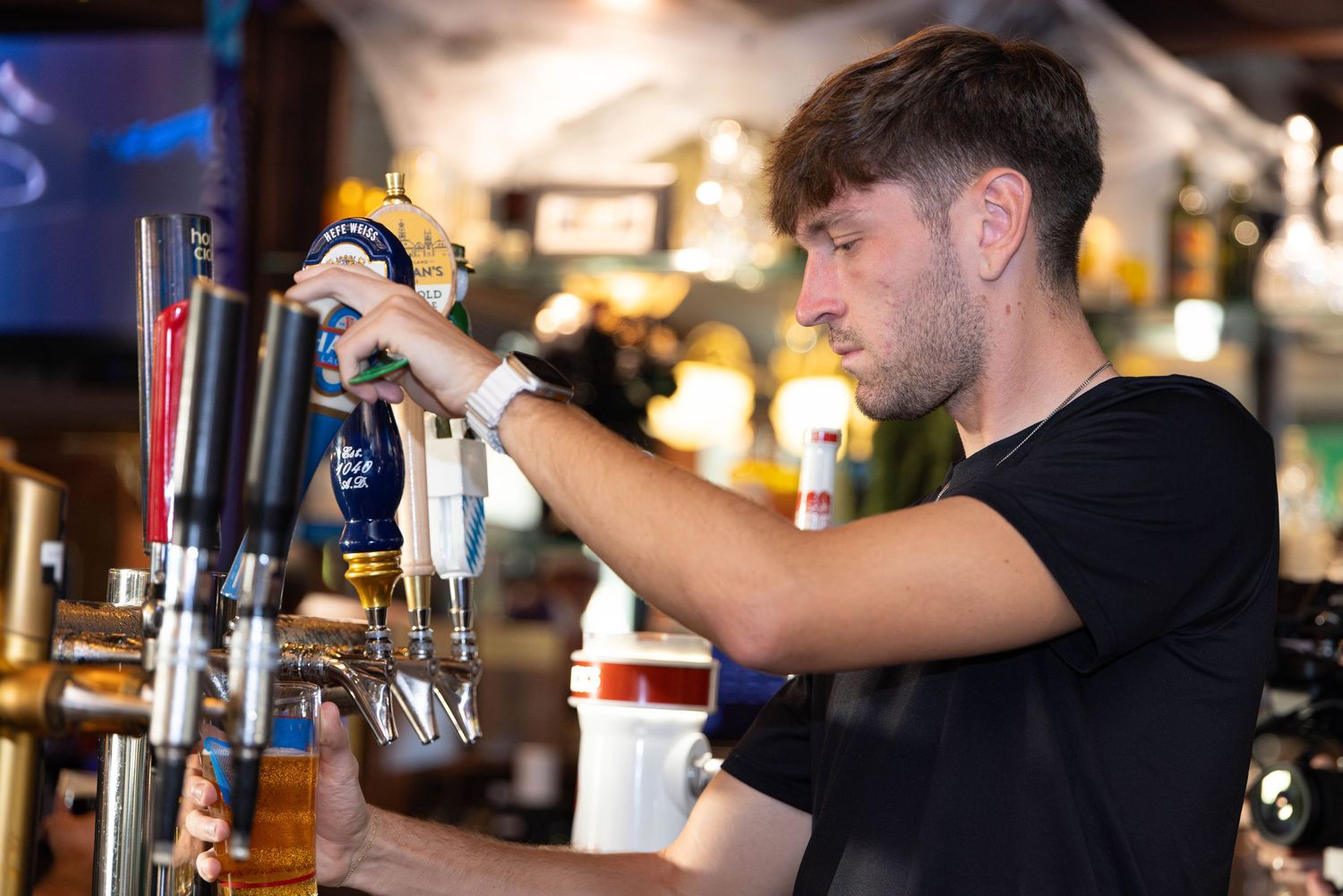 Bartender pouring draft beer from tap at a pub bar counter.