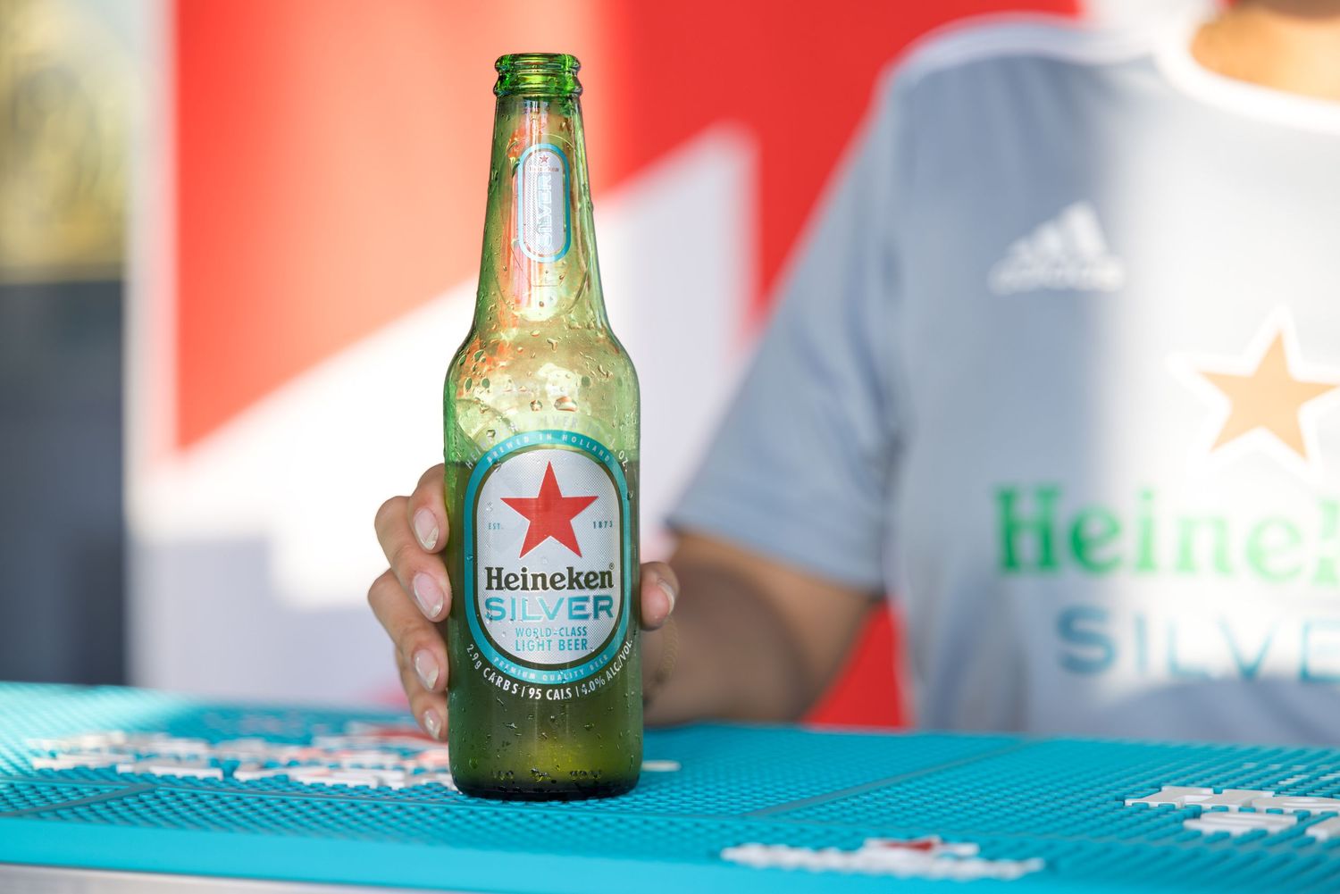 Cold Heineken beer bottle with condensation against a red background.