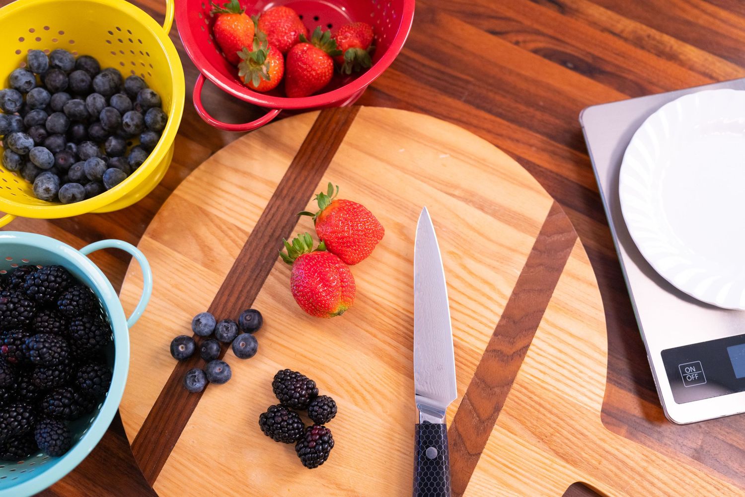 Fresh berries including blueberries, blackberries and strawberries on a wooden cutting board with a knife.