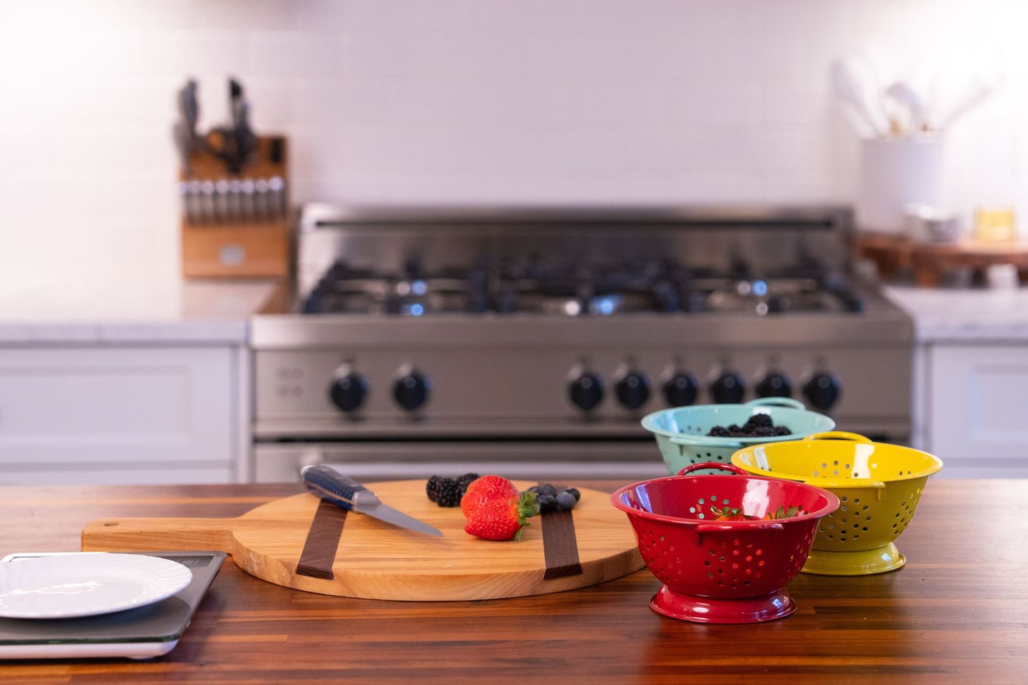 Modern kitchen counter with colorful bowls and a wooden cutting board near a stainless steel stove.