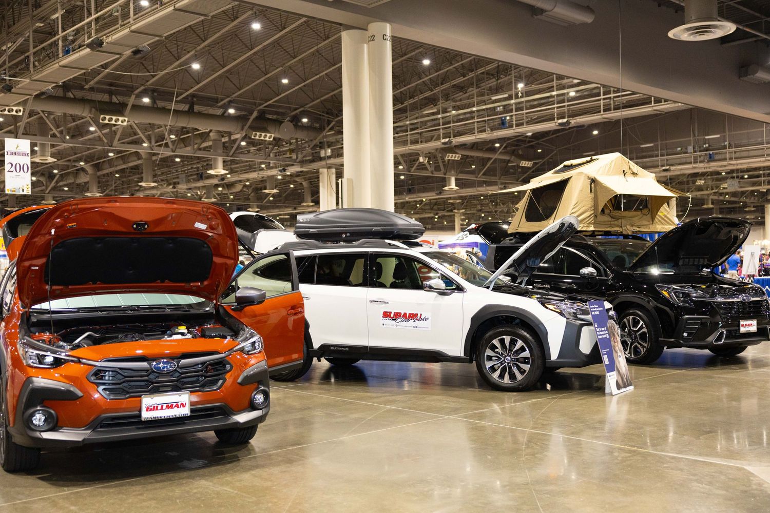 New cars on display at an auto show with orange, white and black vehicles in a large showroom.