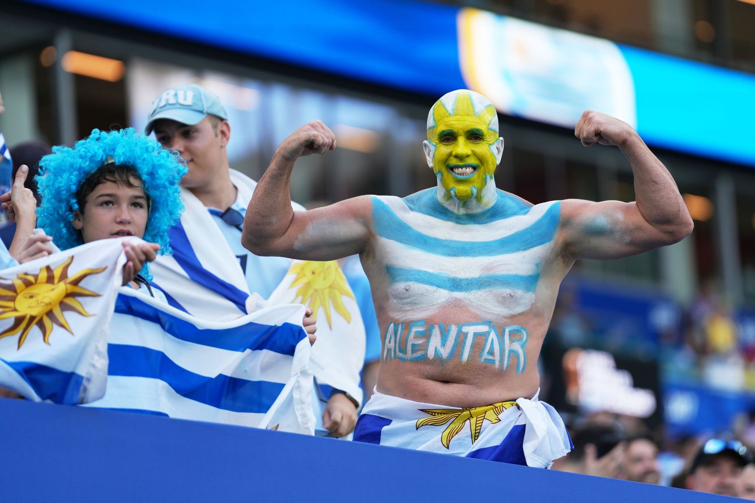 Uruguay soccer fans with painted bodies and flags cheering enthusiastically in the stadium stands.
