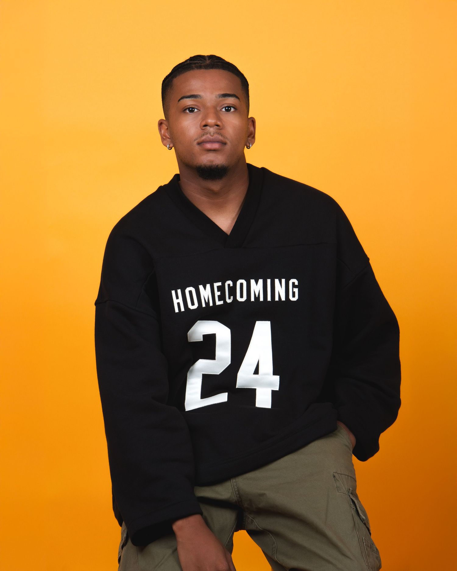 Portrait against orange background wearing black Homecoming 24 sweatshirt.