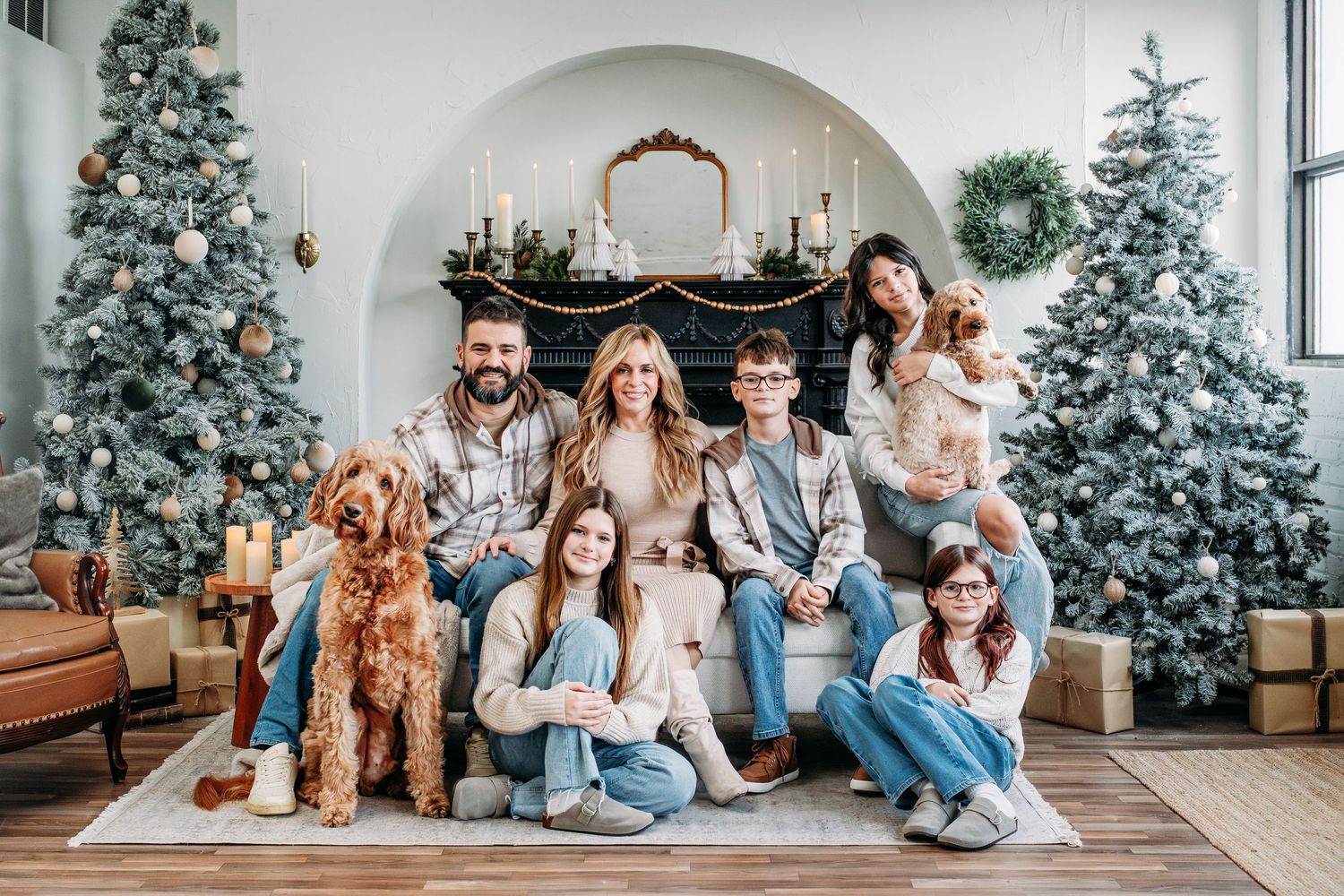 Holiday family photo with Christmas trees and festive decor in bright interior.