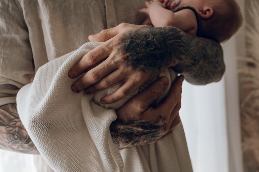A person holding an infant wearing a white onesie against a light background.