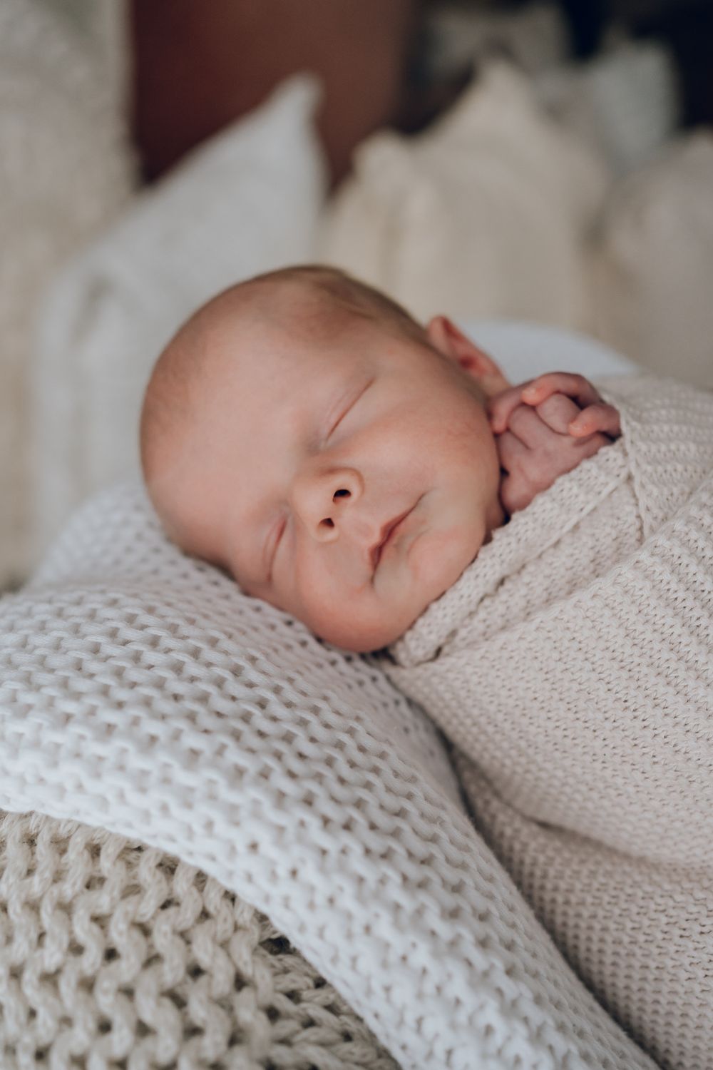 Sleeping newborn wrapped in cozy knit blankets in neutral tones.