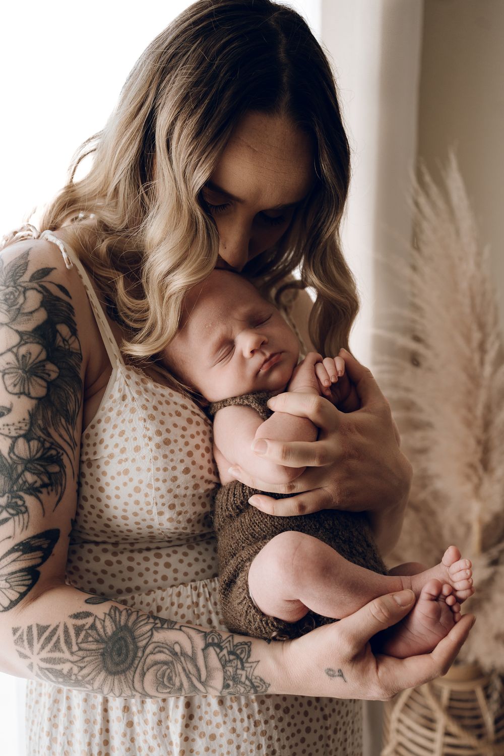 Close-up moments showing tattoos and a white polka dot dress while holding a newborn.