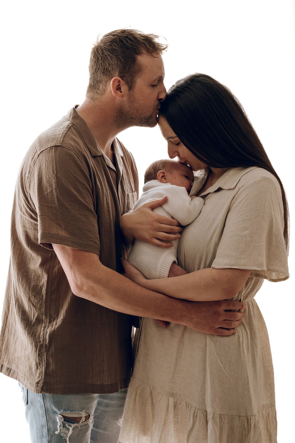 Tender family moment with newborn baby wrapped in white between parents.