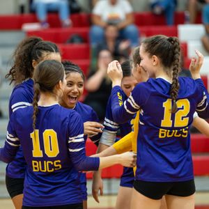 Woman athletes in purple Bucs jerseys celebrate together during a volleyball game, showing team spirit and excitement.