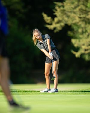 A golfer in athletic attire takes aim and prepares to putt on a sunny green course.