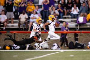 Football player in yellow uniform runs up the sideline during a high school football game as defender dives to make tackle.