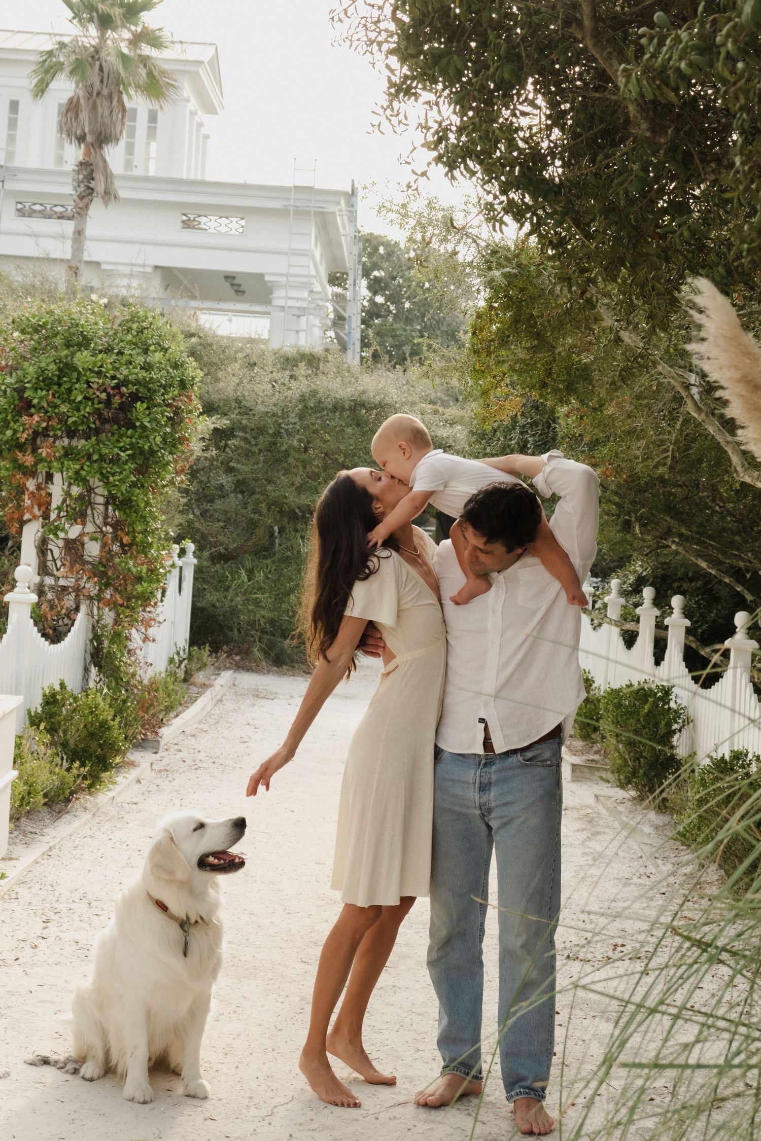 A couple and their white dog share playful moments in a garden pathway.