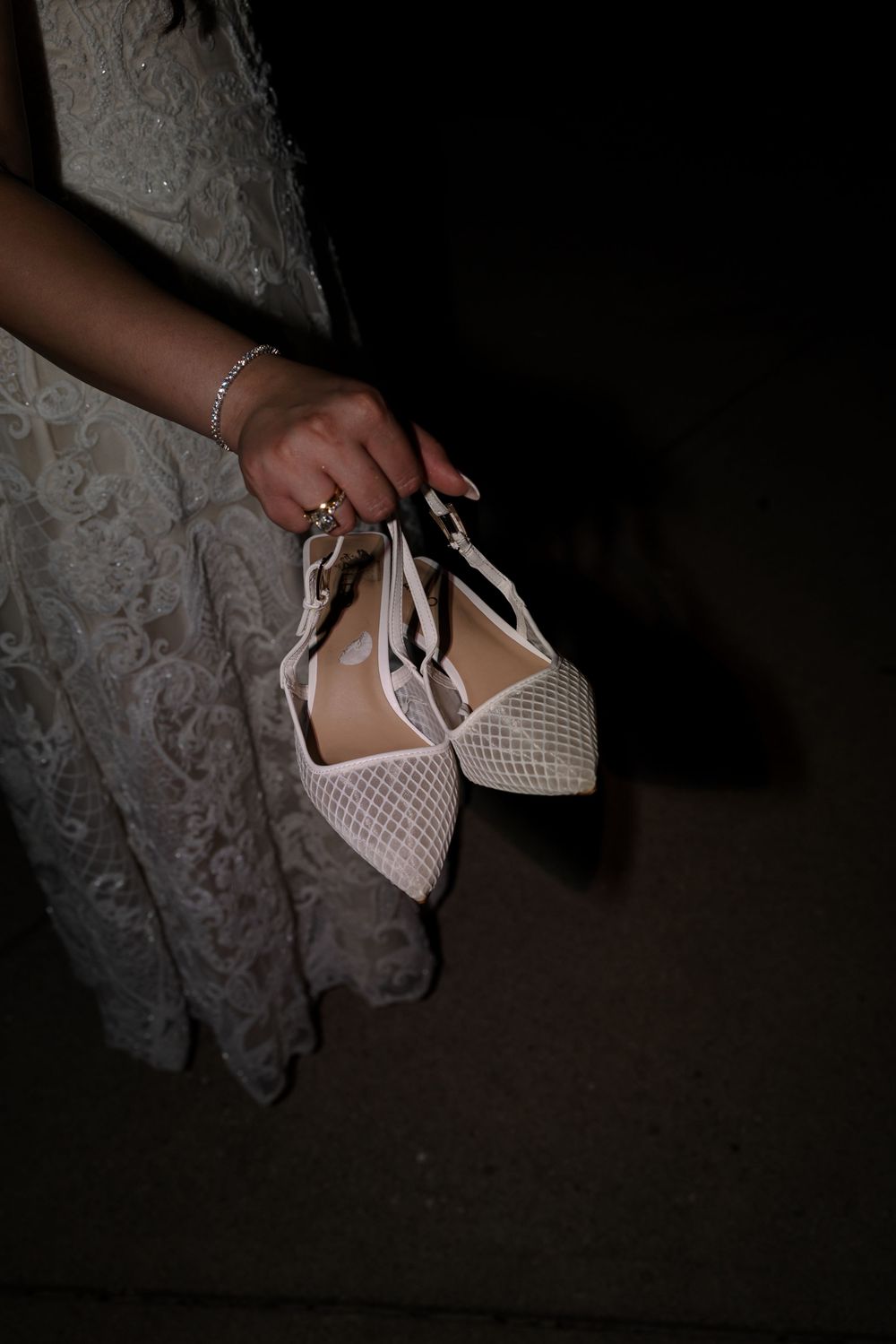 White perforated leather flats with bow details against a patterned lace backdrop.