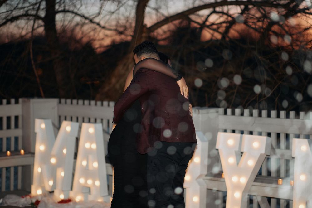 A silhouetted couple embraces in front of glowing marquee letters during a romantic evening.