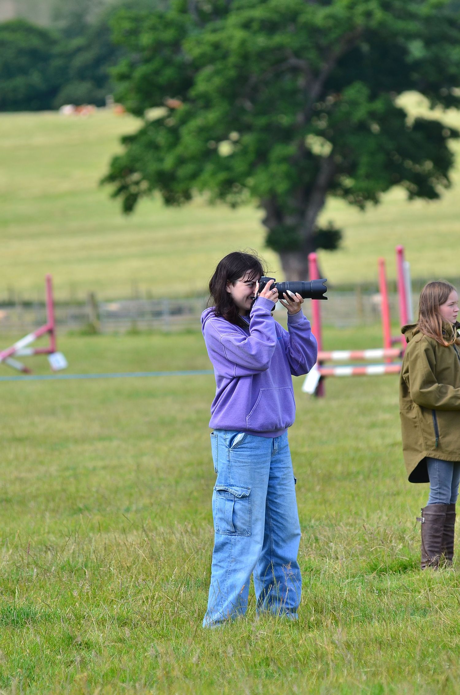 A photographer wearing purple takes pictures in a grassy field with camera equipment.