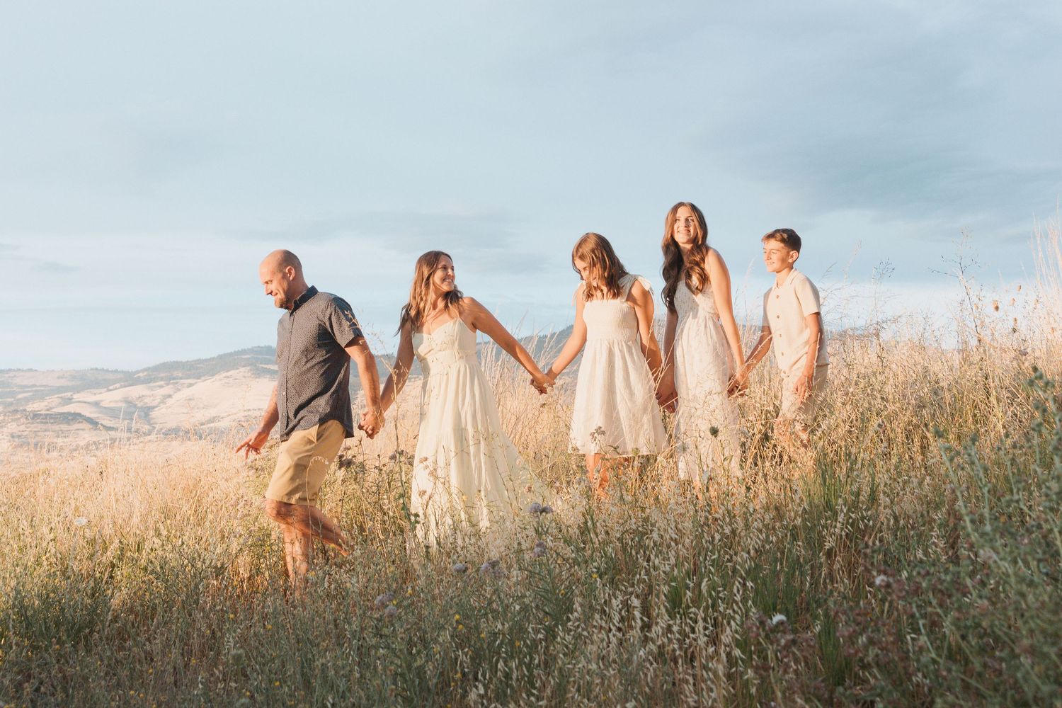 A group walks together through a golden field at sunset wearing flowing white dresses.