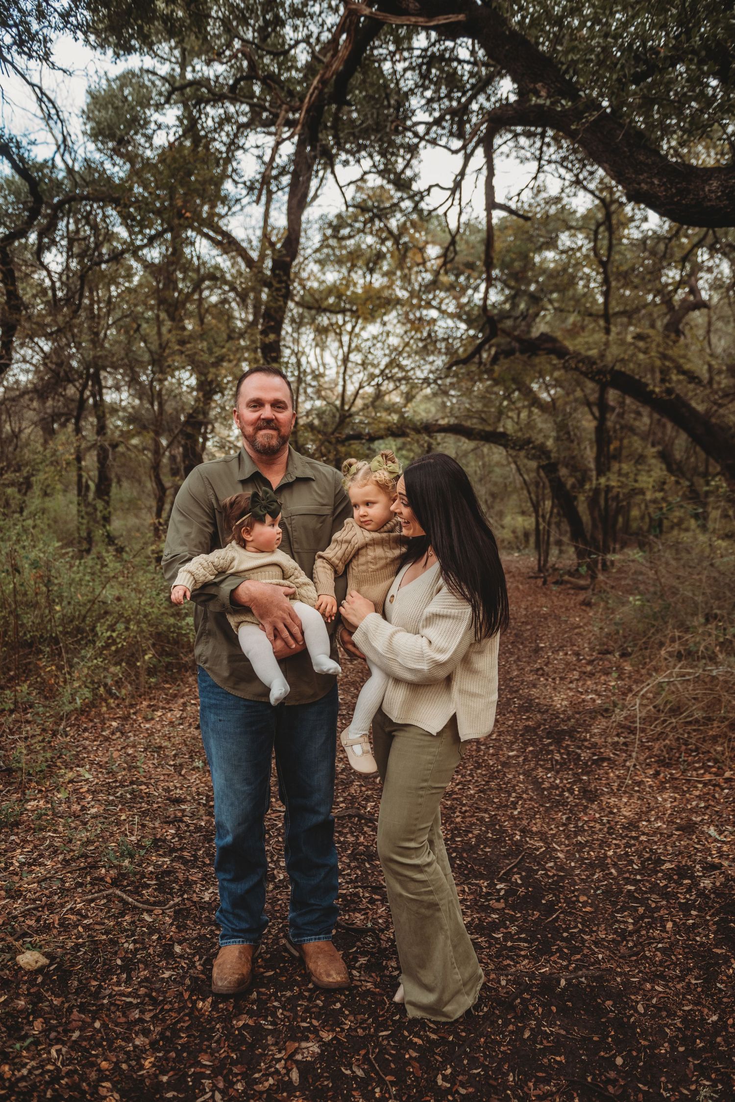 A family enjoying an autumn day together while standing on a wooded trail covered in fallen leaves.