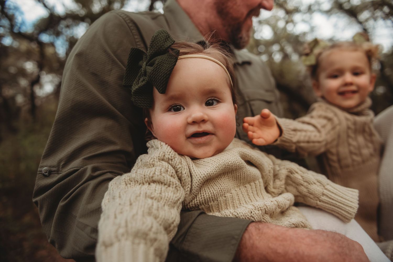 A baby in a cozy cream sweater is held outdoors during autumn with blurred background.
