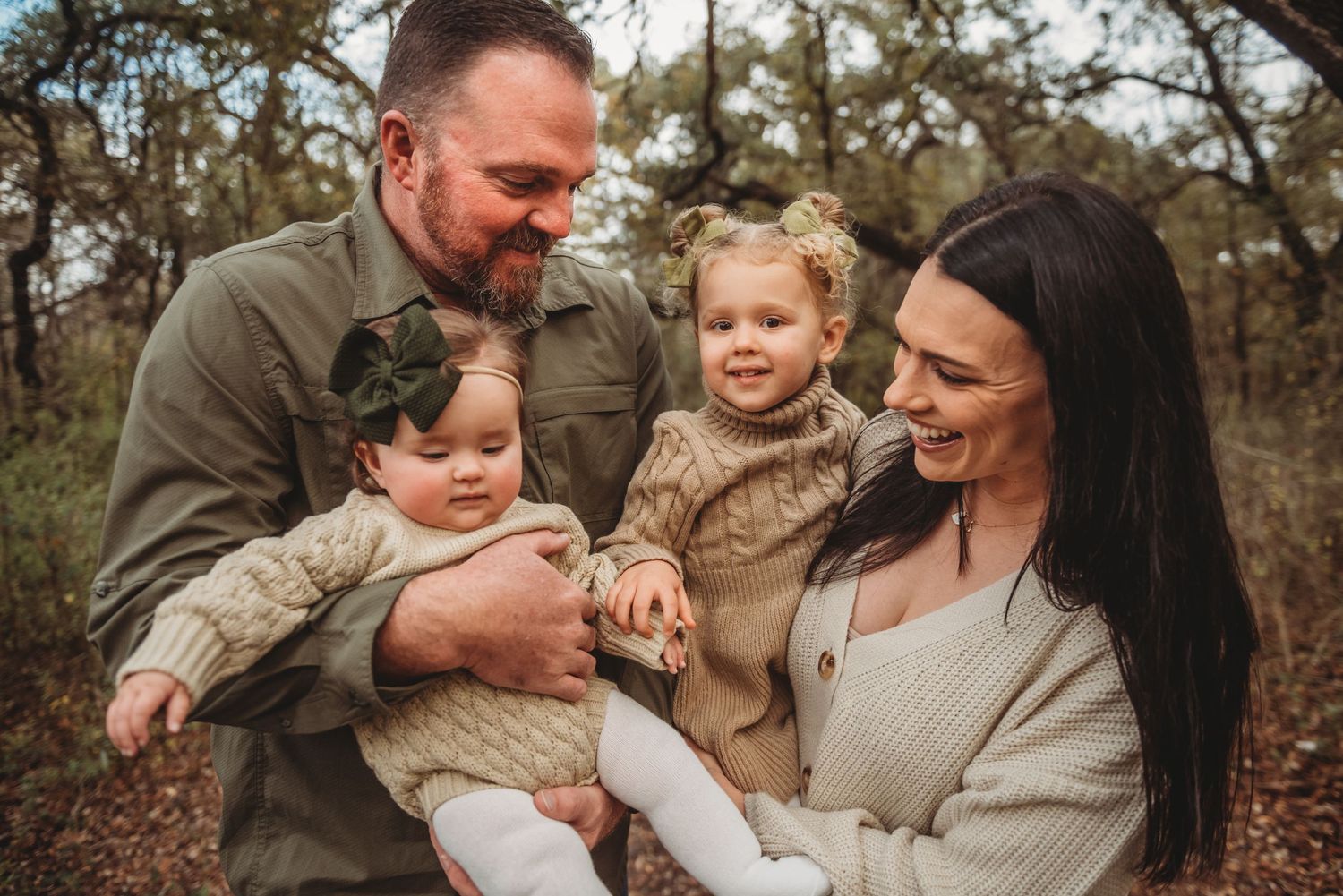 A family in neutral toned sweaters shares a joyful moment together outdoors during an autumn photo session.
