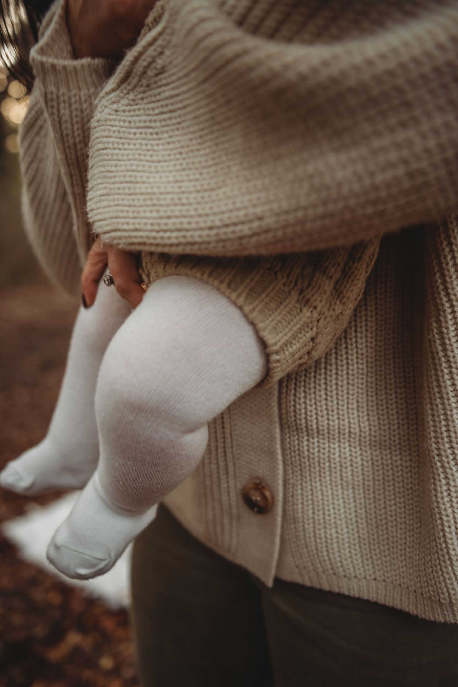 Close-up of baby legs wearing white socks and a cozy beige knit cardigan sweater in autumn setting.