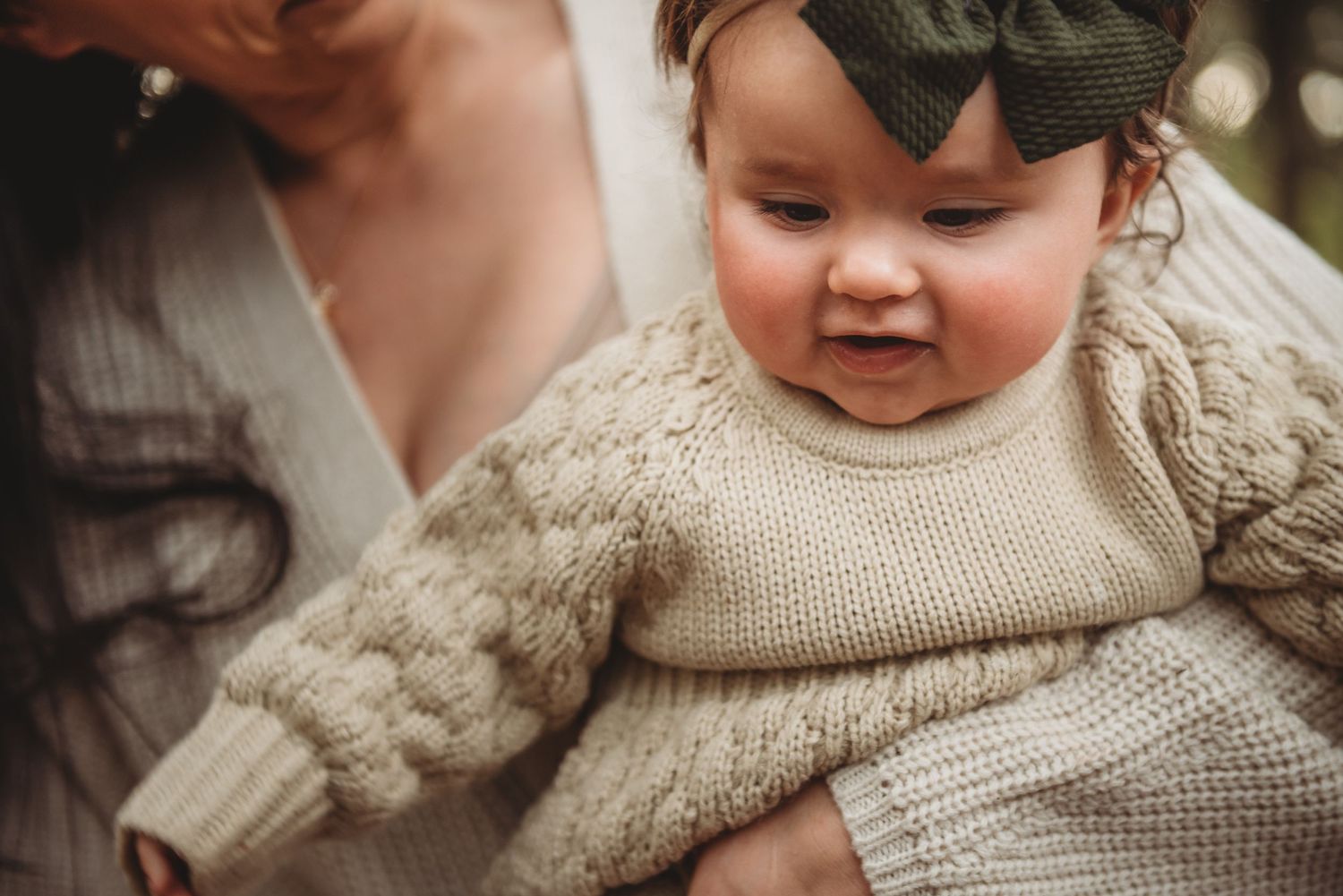 Baby wearing a cozy cream knit sweater smiles while being held outdoors.