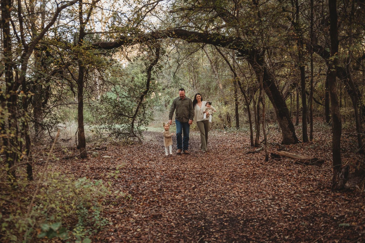 A couple takes a scenic walk through a wooded autumn trail covered in fallen leaves.