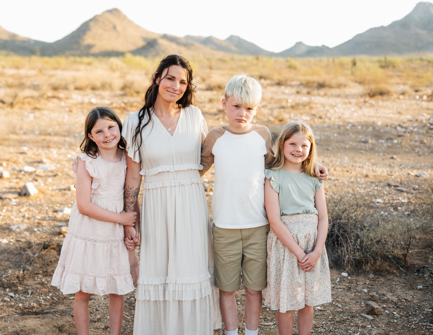 Family of five posing together in desert landscape with mountains and brush in background.