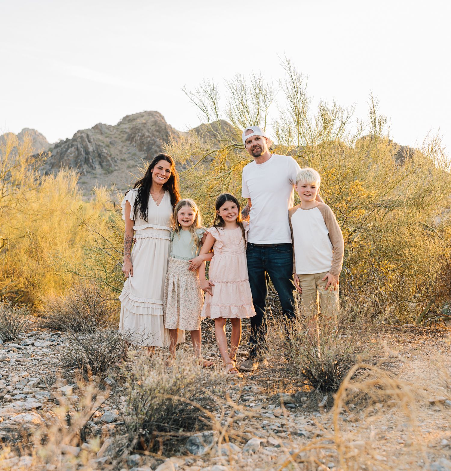 Family of five posing together in desert landscape with mountains and brush in background.