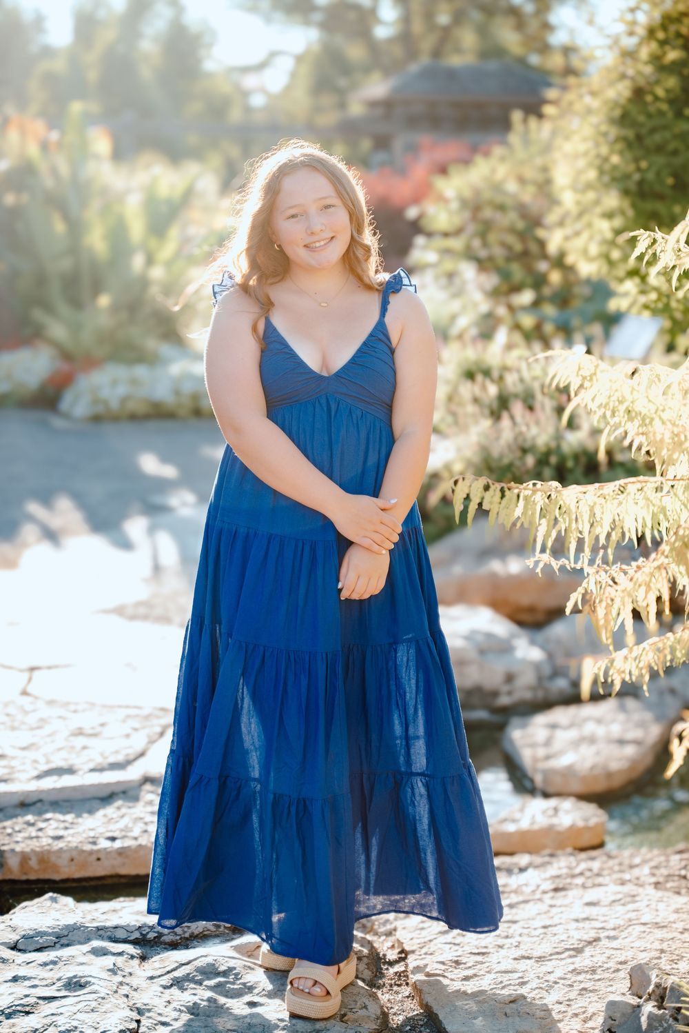 Beautiful blue tiered maxi dress on display in natural outdoor setting with sunlit rocks and foliage.