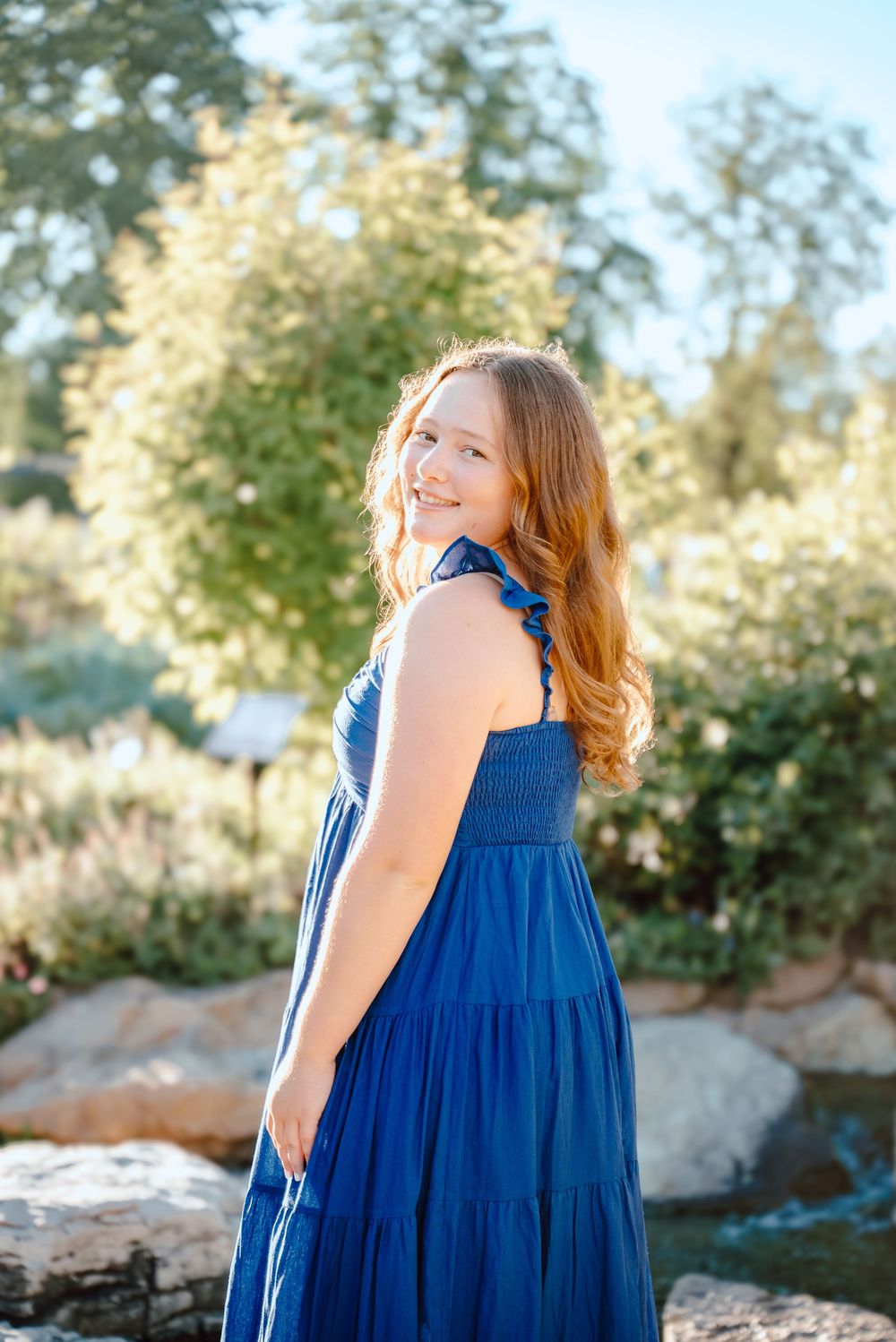 Elegant royal blue maxi dress with ruffle straps shown in scenic garden setting with golden sunlight.