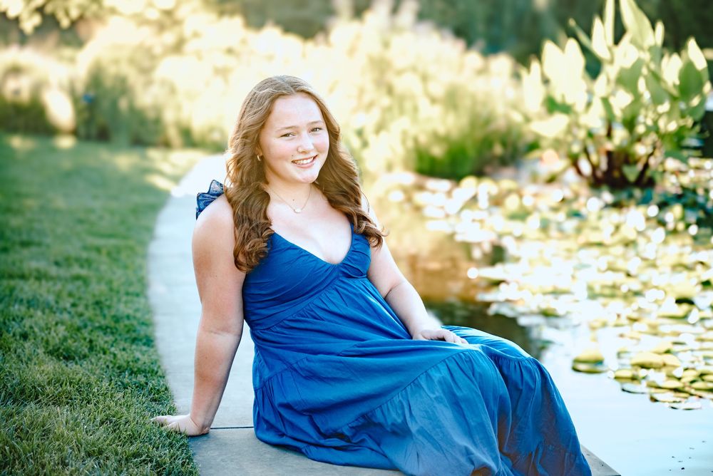 A summer portrait by a pond featuring someone in a royal blue dress sitting at the water's edge.
