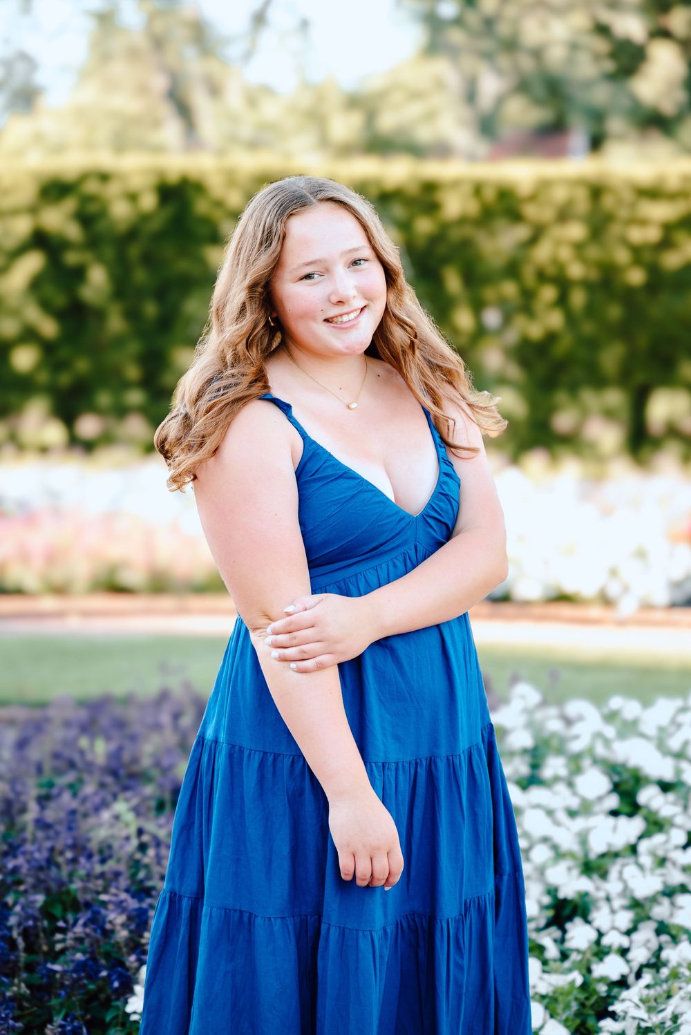 Natural outdoor portraits taken near blooming flowers with person in vibrant blue tiered dress.