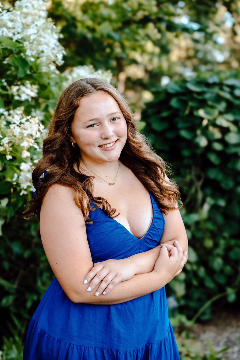 A garden portrait with white flowering bushes featuring someone in a deep blue tiered dress.