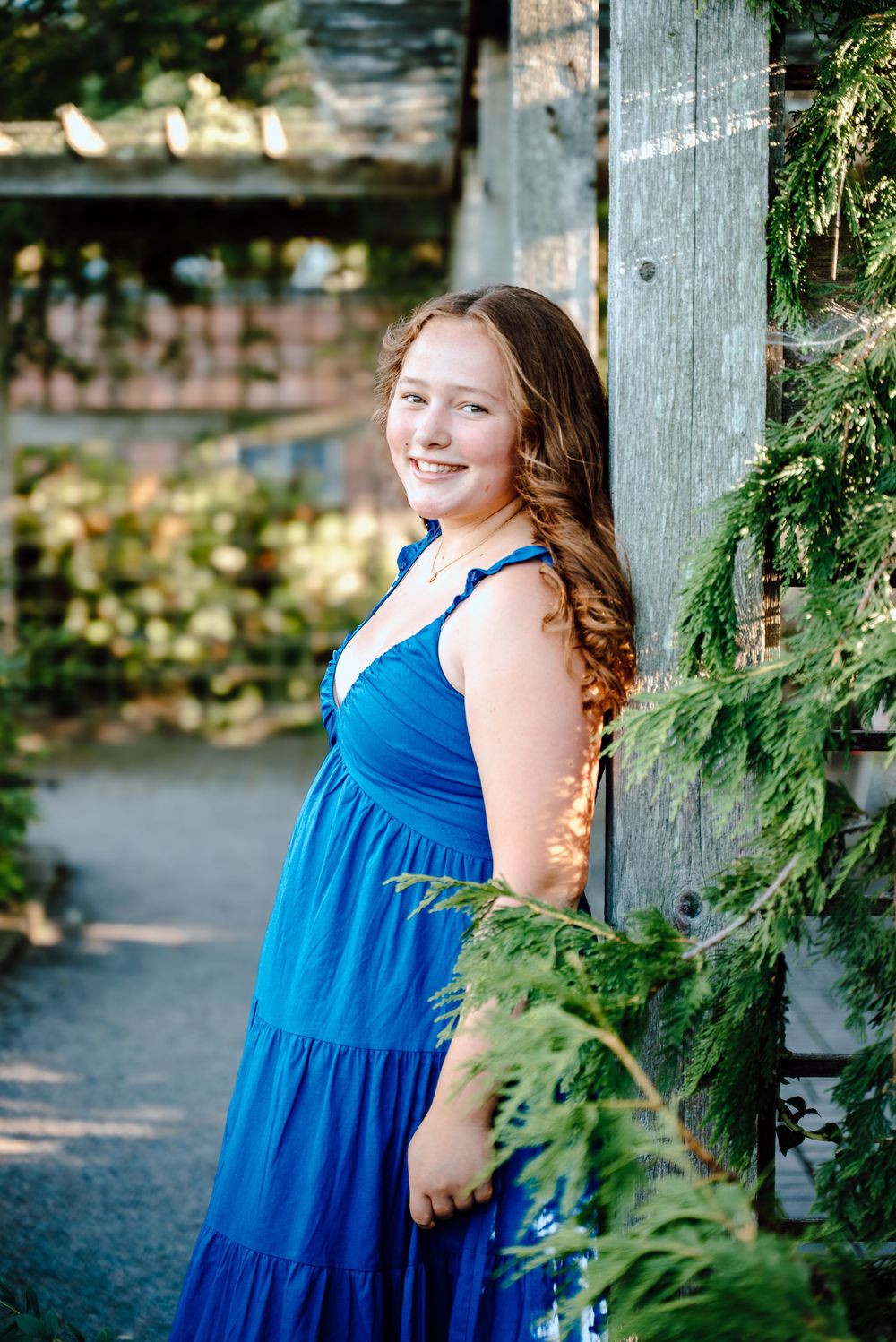 A rustic wooden post frames a garden scene with someone in a bright blue dress amid greenery.
