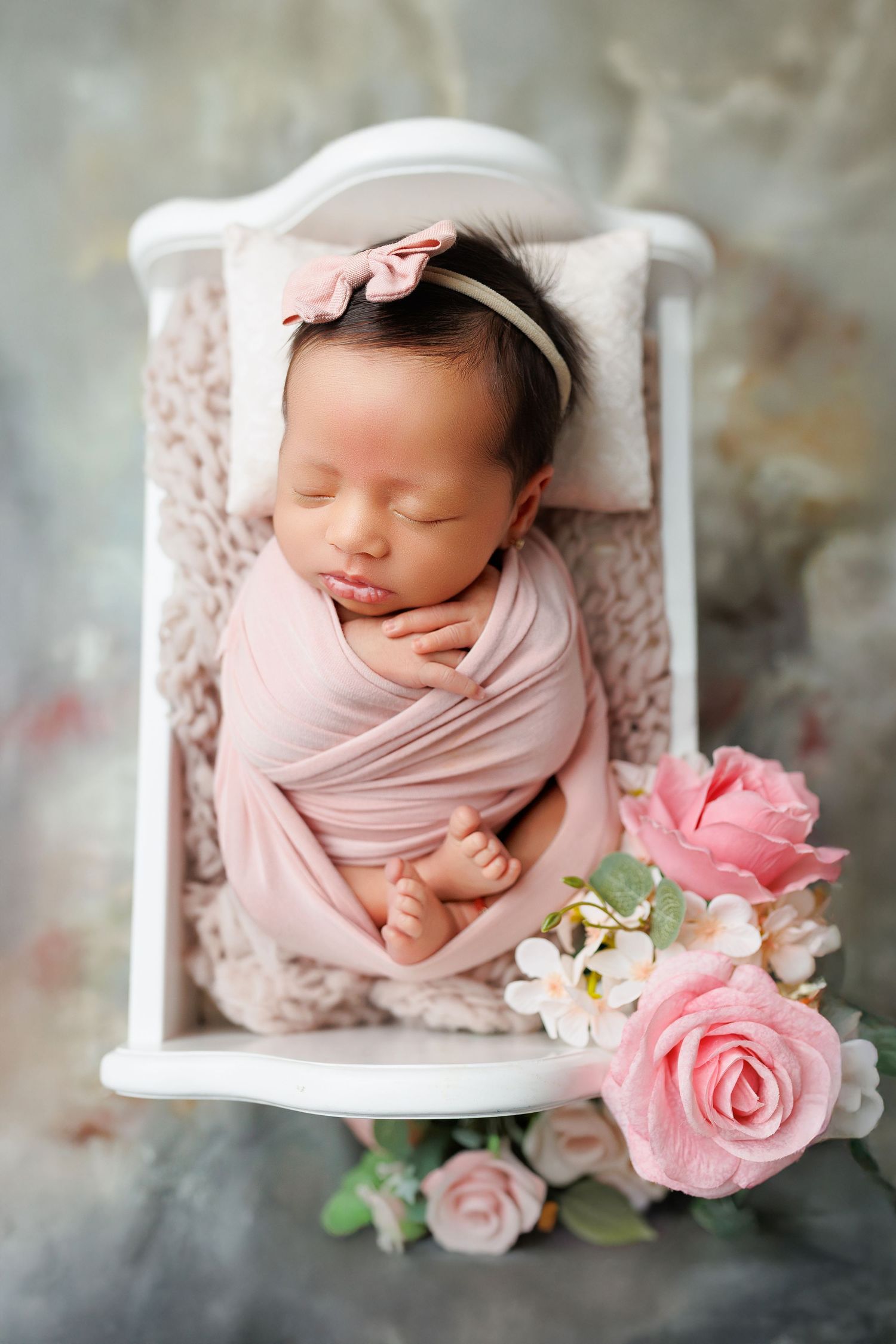 Newborn photography collage with baby wrapped in pink swaddle alongside delicate pink roses and white flowers in soft lighting.