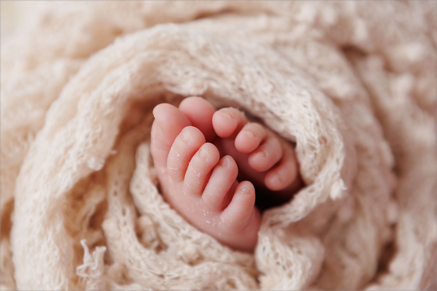 Tiny baby feet peeking out from cream colored knit blanket.