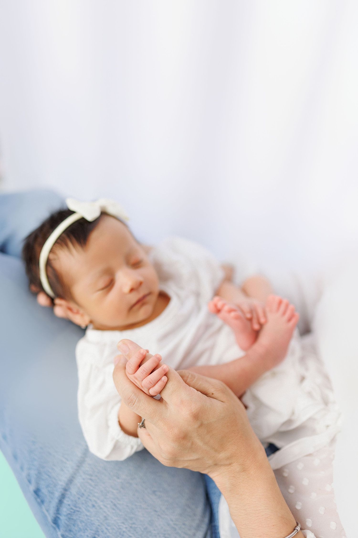A sleeping newborn baby wearing white lies on a blue blanket while gentle hands tenderly hold their tiny feet.