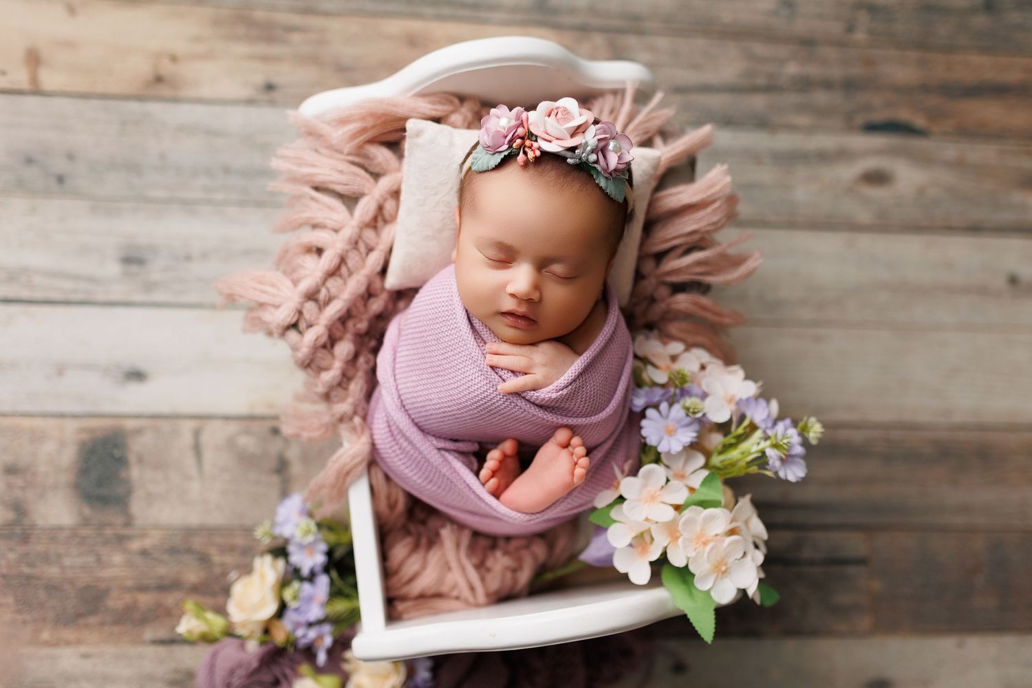 A newborn baby sleeping peacefully in a rustic wooden setting surrounded by delicate purple and white flowers.