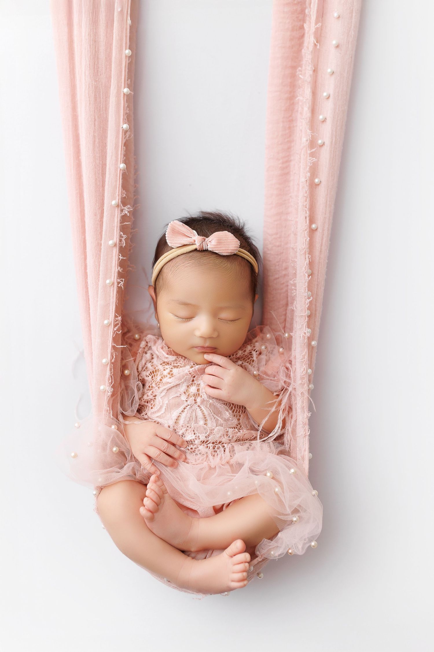 Sleeping newborn in pink tulle dress lying on soft pink fabric in studio photography setup.